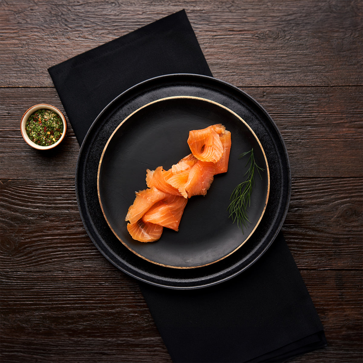 Sliced Native Hebridean Scottish smoked salmon served on a black plate with herbs and seasoning